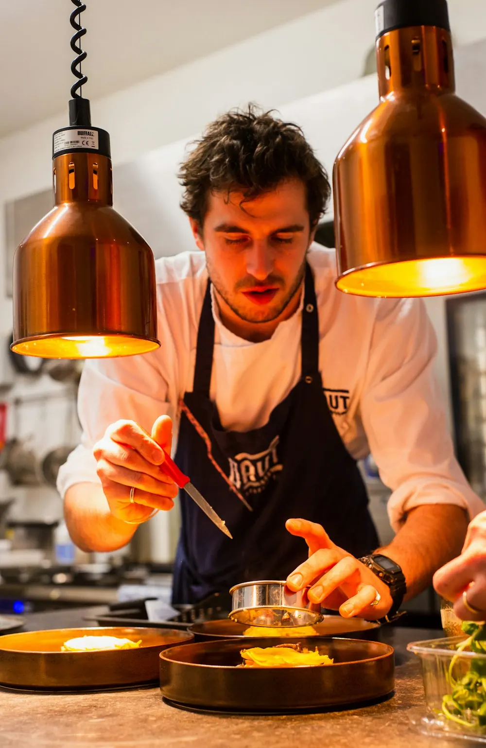 Le chef dresse une assiette sous les lampes chauffantes en cuivre
