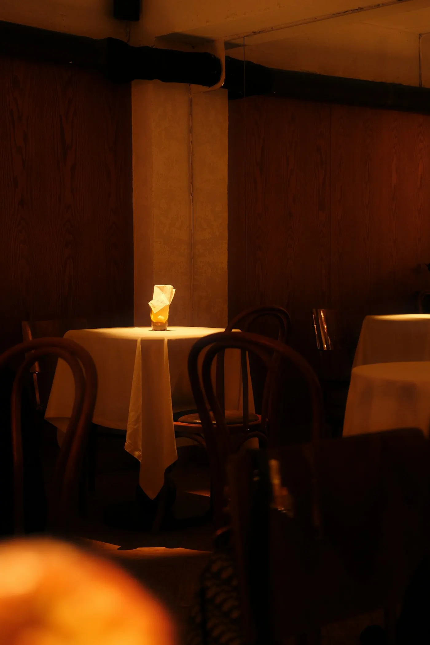 Une table nappée de blanc éclairée par une bougie, dans une salle aux murs de bois sombre