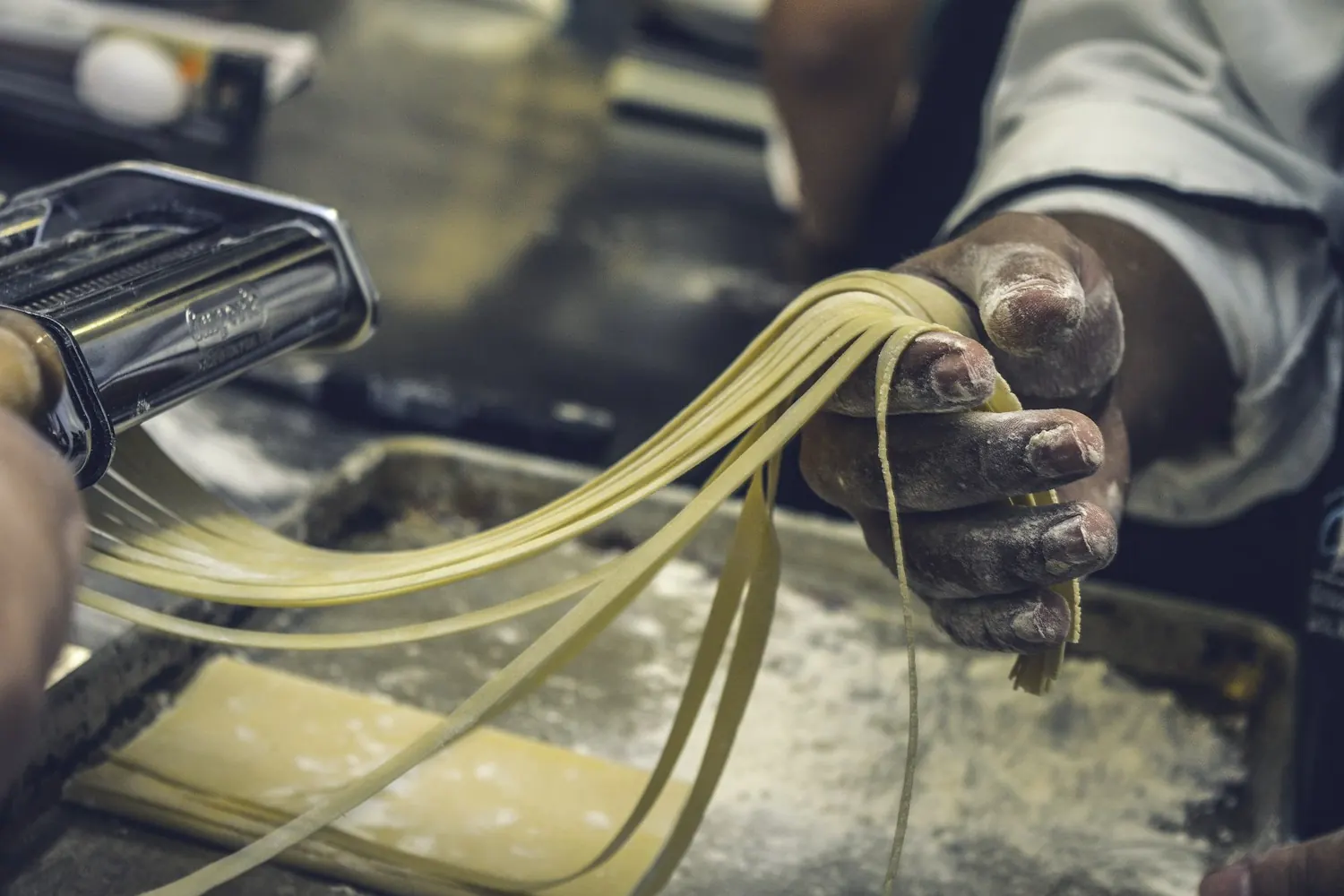 Des mains farinées tirent des pâtes fraîches à la machine
