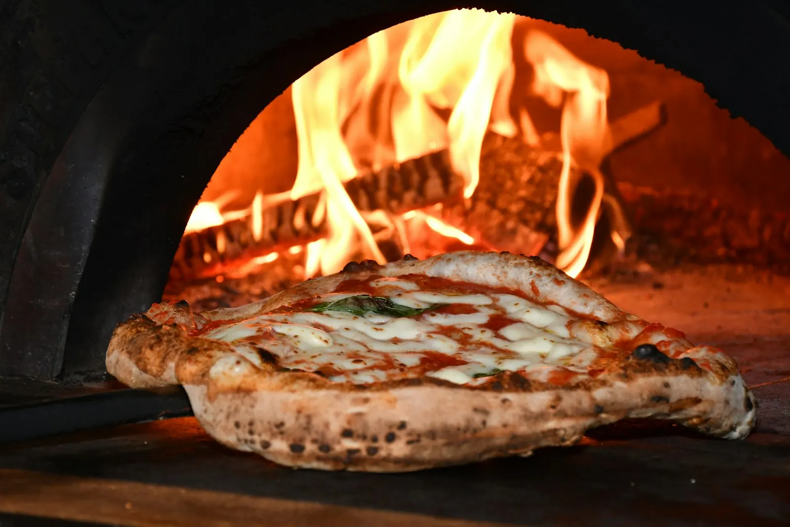 Pizza margherita à la sortie du four à bois, flammes en arrière-plan