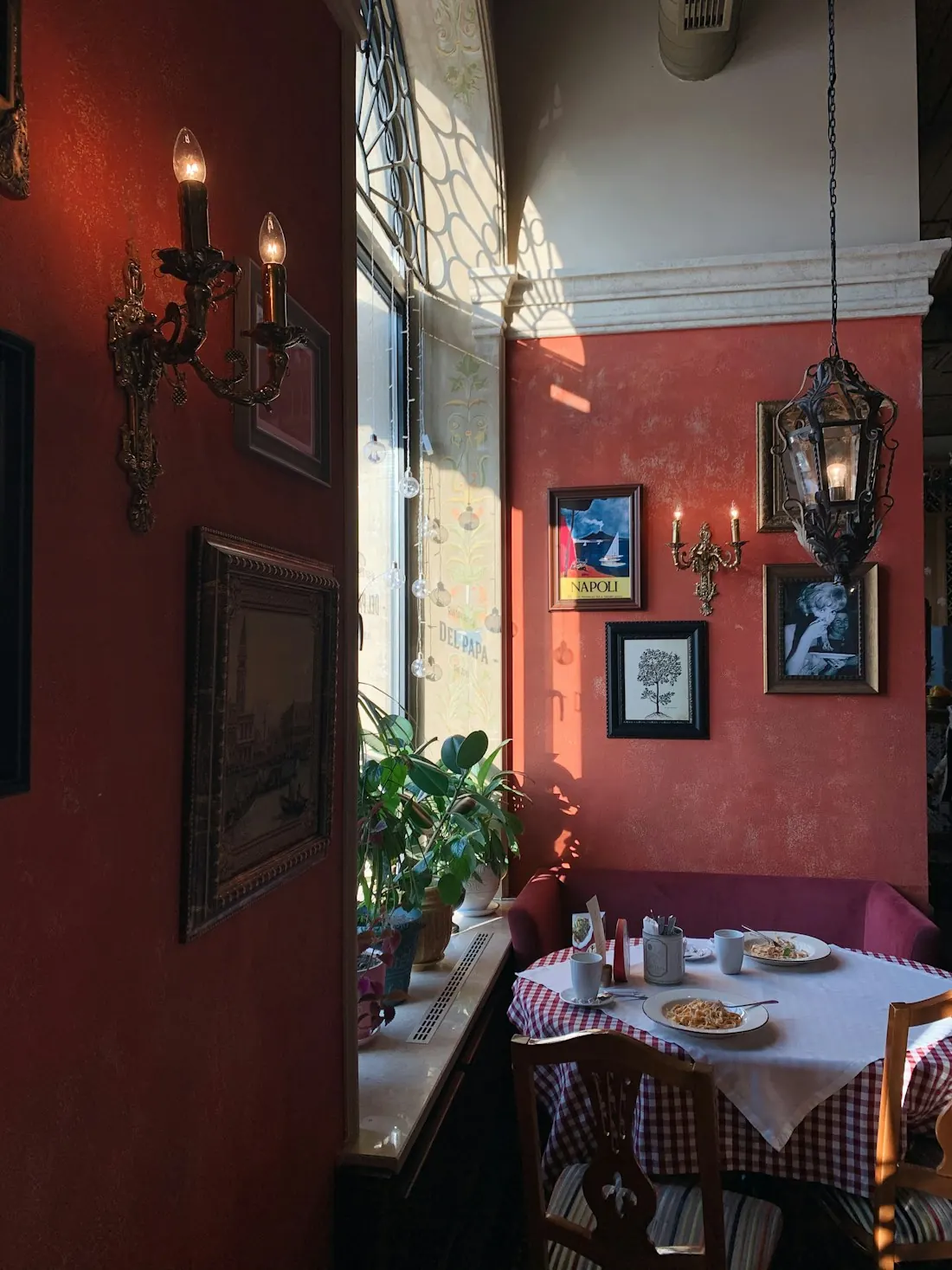 Un coin de salle aux murs rouges, des appliques, une nappe à carreaux près de la fenêtre