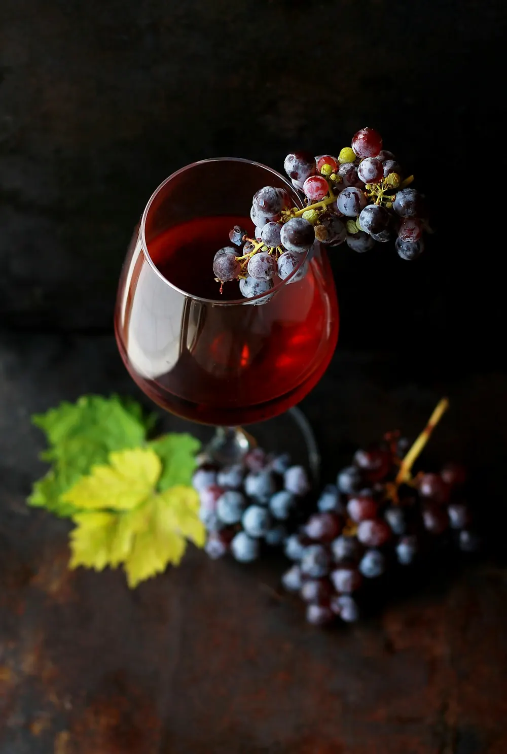 Un verre de vin rouge et une grappe de raisin sur un fond sombre